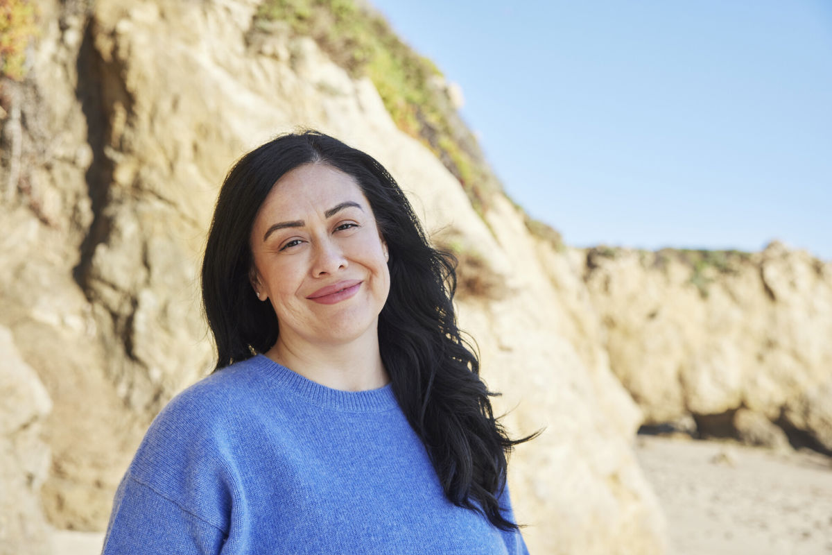 Frau am Strand mit blauen Pullover und schwarzen Haaren lächelt